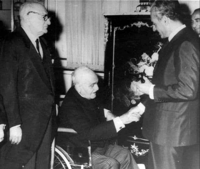 اینجا در این عکس، تقی‌زاده در آستانه ۹۰ سالگی است که دچار فلج پا شده و به اجبار بر رویِ صندلی چرخ‌دار نشسته است. چند سال قبل در بزرگداشت او در دانشگاه کمبریج در لندن (۱۹۶۲م/سال ۱۳۴۱ش)، بزرگ‌ترین اندیشمندان ایران‌شناس فرنگی اعتراف کردند که هیچ چیزی برایِ تقدیم به او نداریم که به معنایِ راستین لیاقت او را داشته باشد. با همین اعتراف بعد از سخنرانی والتر برونو هنینگ و هارولد بیلی دو ایران‌شناس برجسته در وصف تقی‌زاده، کتاب مجموعه مقالات ایران‌شناسی خود (۳۱ مقاله از خاورشناسان به‌نام) به سه زبان فرانسه، آلمانی و انگلیسی با عنوان «رانِ ملخ» را به او پیشکش کردند. به‌کارگیری اصطلاح «این رانِ ملخ تقدیم تو»‌ در زبان فارسی به اظهار تواضع و فروتنی اشاره دارد (که ریشه تاریخی آن به داستان سلیمان نبی برمی‌گردد)؛ یعنی هدیه‌ای که اگرچه به فردی داده می‌شود، ولی این هدیه در خور شان و مقام/جایگاه گیرنده هدیه نیست. حالا با این اوصاف، دردناکی این عکس در این است که محمدرضا پهلوی حتی حاضر نیست در برابر بزرگی این آدم (که علامه قزوینی او را حضرت تقی‌زاده می‌نامد) که به ناچار زمین‌گیر هم شده، کمی خم شود و از بالا با او دست ندهد.