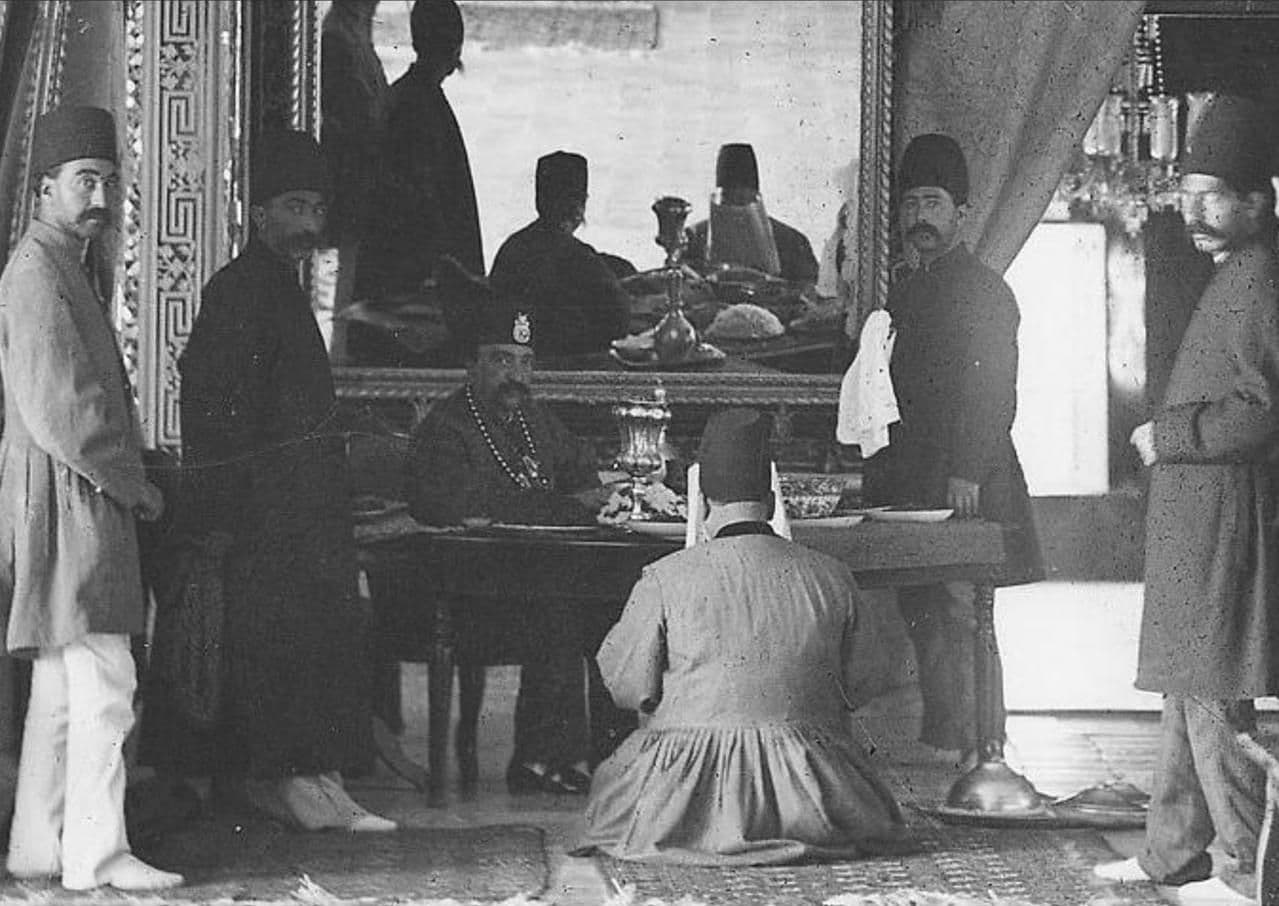 محمدحسن‌خانِ اعتمادالسلطنه -که رویِ زمین نشسته- برایِ ناصرالدین‌شاه در كاخ صاحبقرانيه روزنامه می‌خواند. او وزیر انطباعات (چاپ‌ونشر) و مترجم مخصوص شاه بود و ریاست دارالترجمه همایونی را نیز برعهده داشت. 

اعتمادالسلطنه یک ماه پیش از کشته‌شدنِ ناصرالدین‌شاه، در سن پنجاه‌وسه سالگی به علت سکته قلبی در تهران درگذشت.

*عكس از یوسف‌خان (نام عکاس را به اشتباه آنتوان سوریوگین نوشته بودم، که با تذکر دوست عزیزی آن را اصلاح کردم. گویا خیلی از عکس‌هایی که به‌نام سوریوگین ثبت شده، متعلق به یوسف‌خان عکاس‌باشی دربار ناصری است).